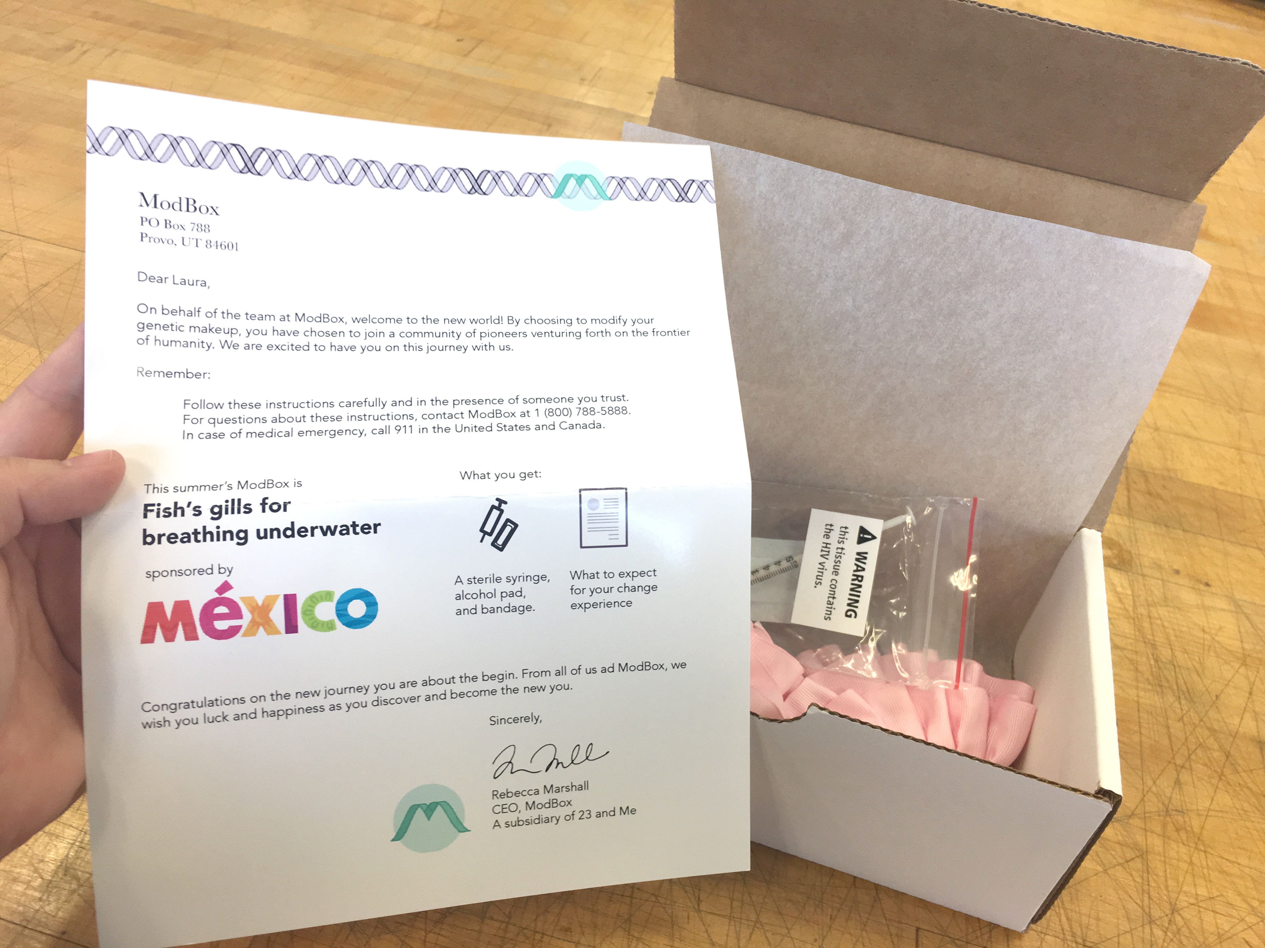 The box is open and includes a letter welcoming the customer to the frontier of humanity. The box includes a syringe and supplies to genetically modify a human with fish gills for breathing underwater. It's sponsored by Mexico tourism.