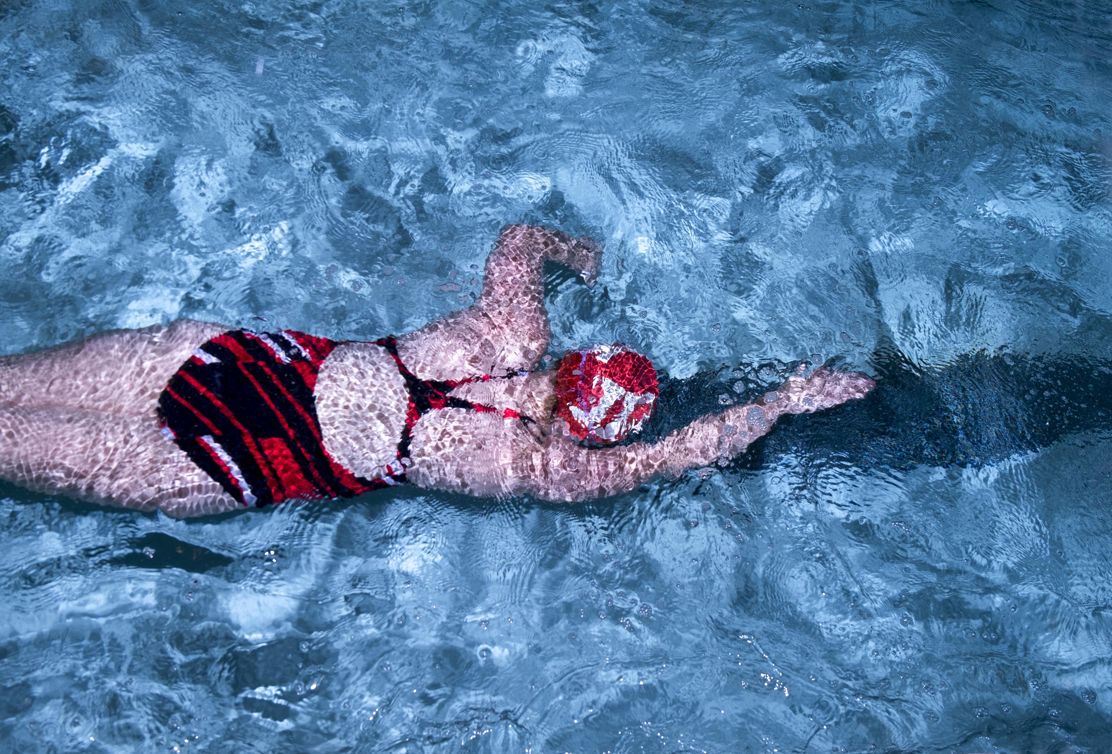 A photograph of a woman in a red swimsuit and a red swimcap, swimming in a pool, shot from above.